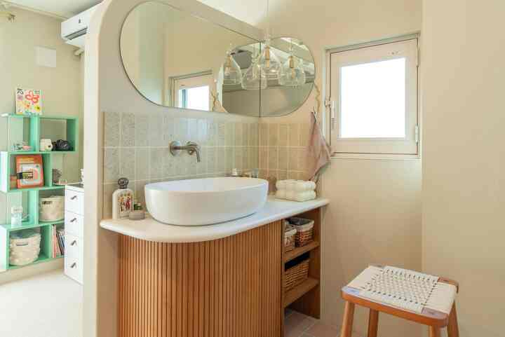 ベージュと木目調のバスルーム、コーナー収納とスツールが配置された自然な雰囲気の空間