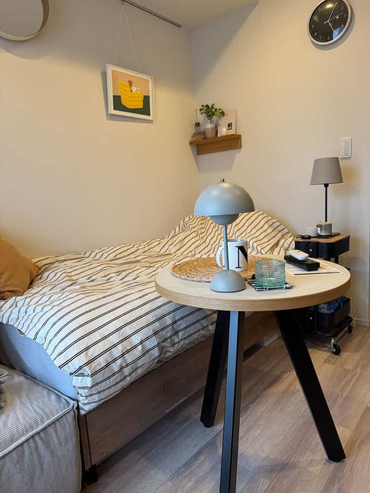 ナチュラルカラーの狭い部屋、ベッドとテーブルランプのある丸テーブルが配置された印象的な空間