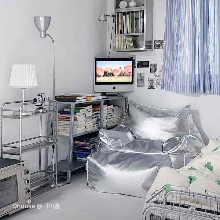 Compact studio apartment living room in silver and gray tones featuring a silver bean bag sofa and bookshelf, modern home office setup
