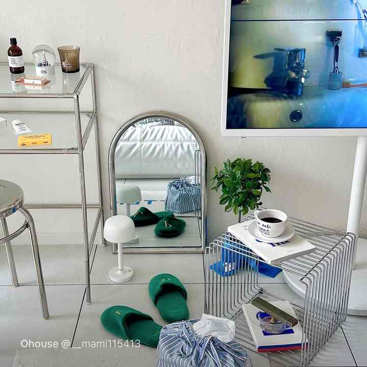 シルバーとホワイトのトーンのリビング、アーチ型の鏡とメタル棚、スリッパとコーヒーカップが置かれたミニマルなインテリア