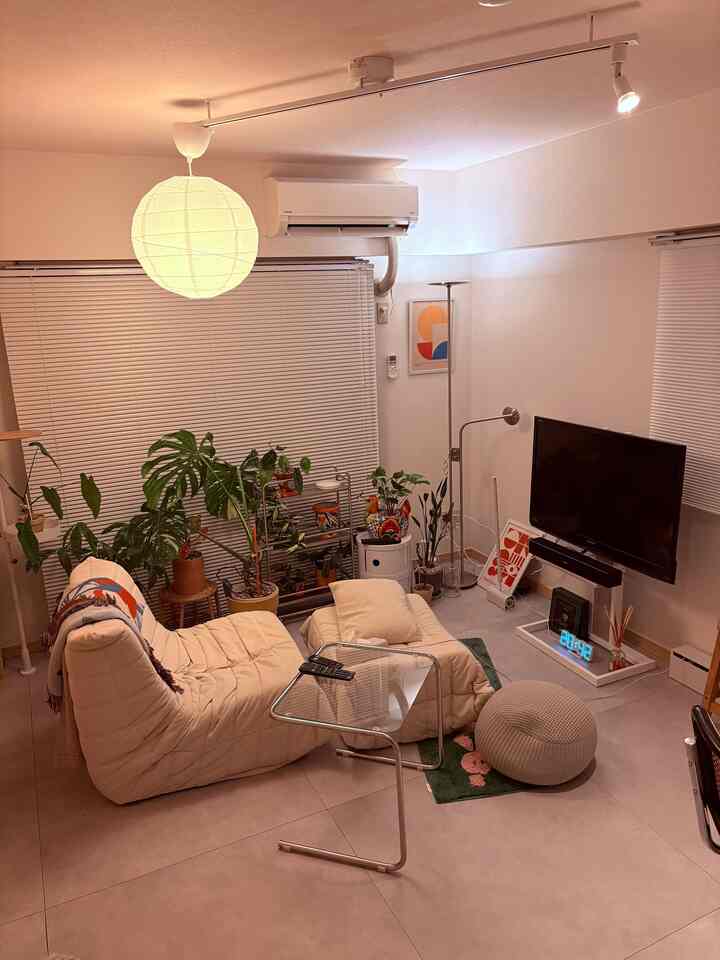 ホワイトとグレーの色調の1LDKリビング、クリーム色のソファとガラステーブル、植物が配置された居心地の良いミッドセンチュリーモダンな空間