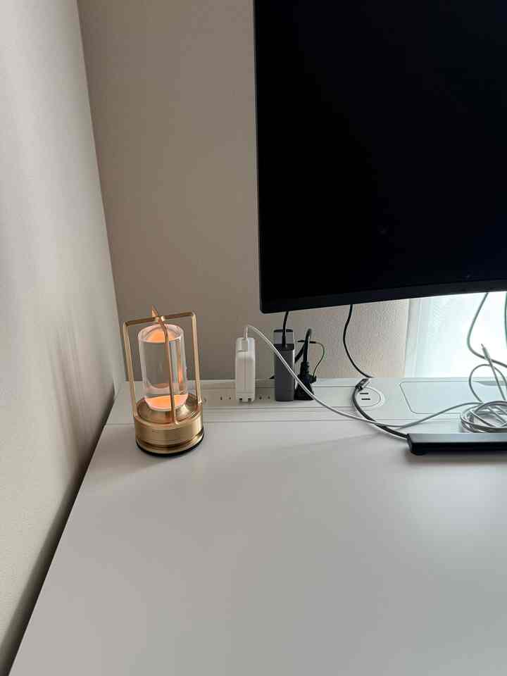 白とゴールドのトーンのホームオフィス空間、机の上にテーブルランプとモニターが配置された整然とした作業スペース