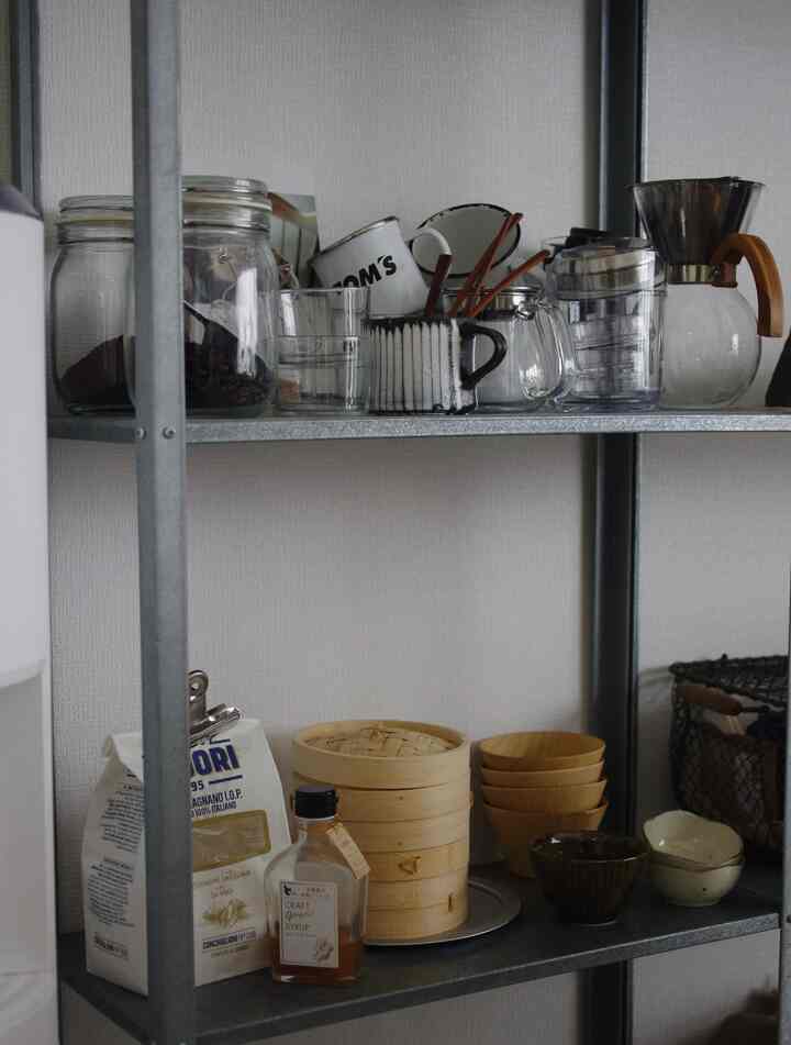 Kitchen shelving space with white walls and gray metal shelf, featuring natural material bowls and coffee tools creating a cozy atmosphere