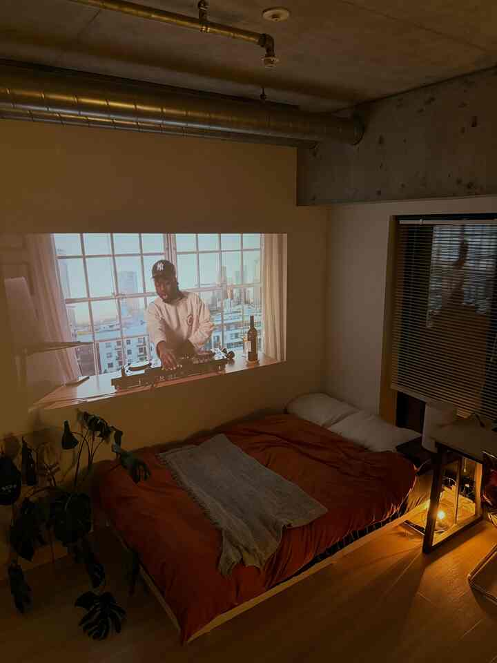 オレンジ色の寝具が配されたコンパクトなモダンな寝室、壁にプロジェクター映像が映し出された雰囲気のある空間