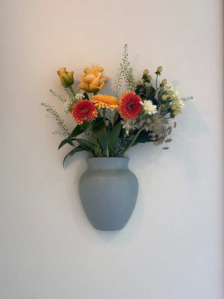Simple entrance space with a blue wall-mounted vase and colorful flowers against a white wall