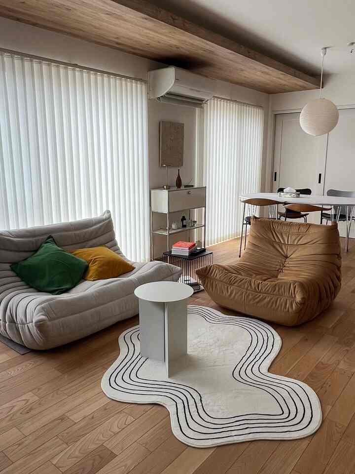 Natural-toned living and dining space featuring two sofas in distinct colors and a uniquely shaped rug in a modern interior