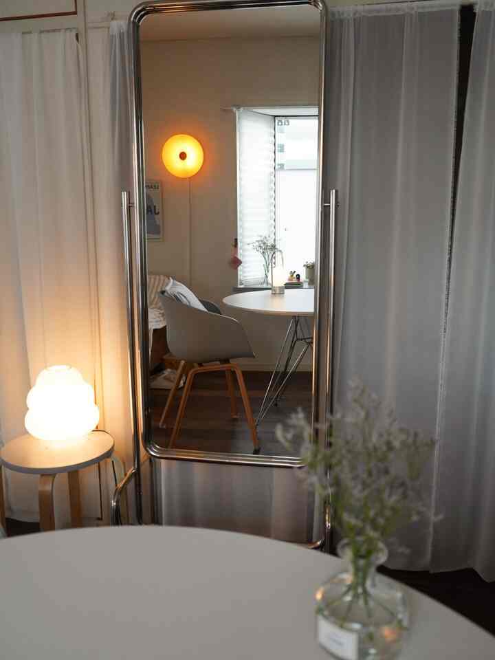 Modern dining room in white and silver tones, featuring a large movable full-length mirror, ambient lighting, and curtains creating a cozy atmosphere