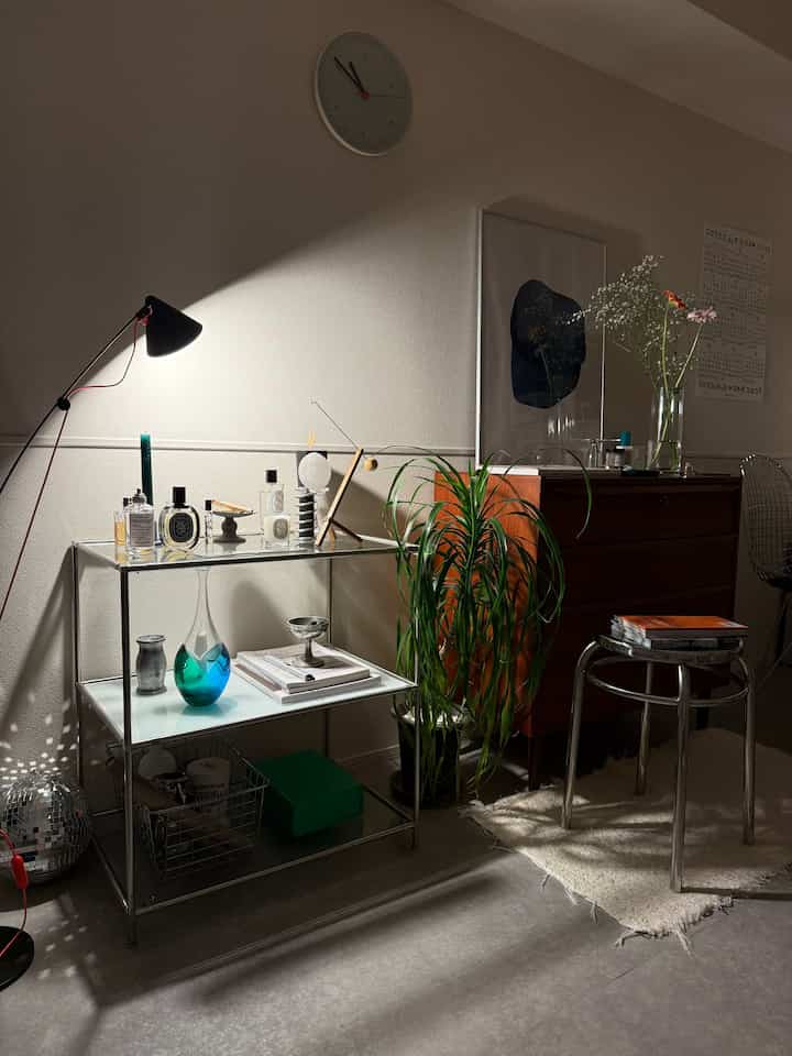 ベージュトーンのリビングルームにシルバーのモジュール家具とヴィンテージの木製チェストが配置され、明るい照明と観葉植物がアクセントになっている雰囲気のあるインテリア