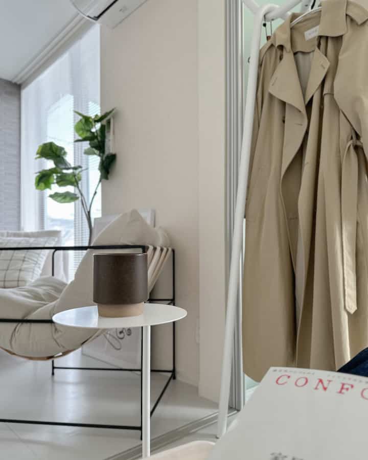 白とベージュのトーンのリビング、コートラック、サイドテーブル、ソファが配置されたシンプルでモダンな雰囲気の空間