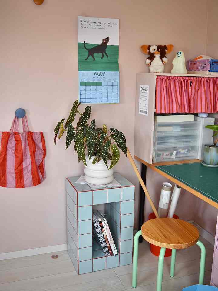 Natural-toned home office with pink walls and sky blue tiled table, featuring a wooden stool and a leafy plant creating a cozy atmosphere