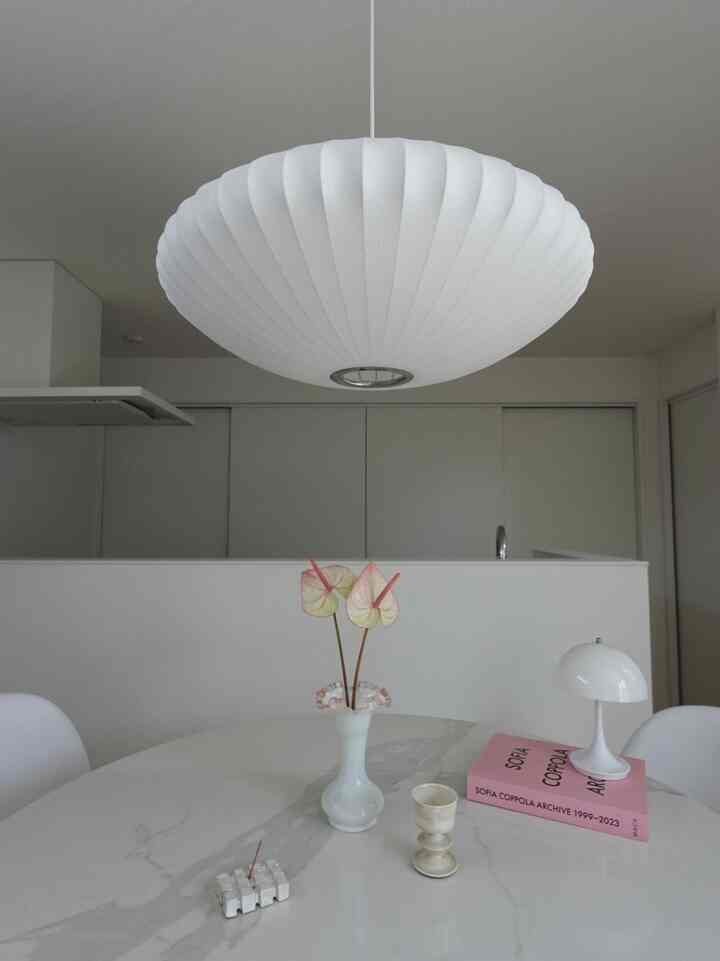 白とピンクの色調のダイニング、中央に花瓶とペンダントライトが配置されたモダンでシンプルな空間