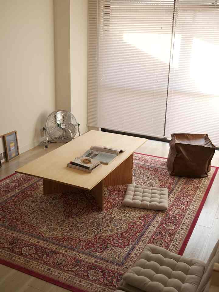 赤いペルシャ風ラグとナチュラルな木製ローテーブルが配置された、ベージュトーンの落ち着いたリビングスペース