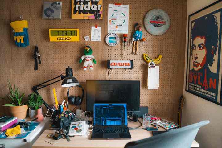 木目調のペグボード壁と机、ノートパソコンやポスターが配置された雰囲気のあるホームオフィス