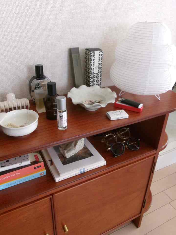 Brown wood tone dresser featuring a white paper stand lamp and assorted decor in a living or multipurpose space