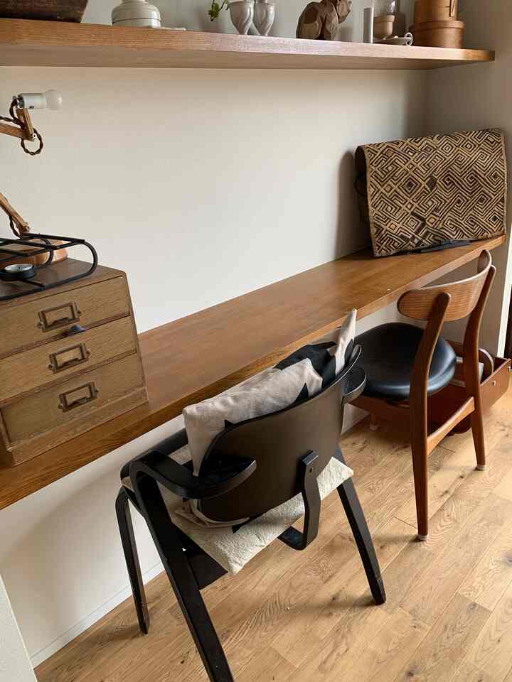 ブラウン調のワークスペース、2つのヴィンテージチェアとクバ布で覆われたモニタースタンドが配置された雰囲気のあるインテリア