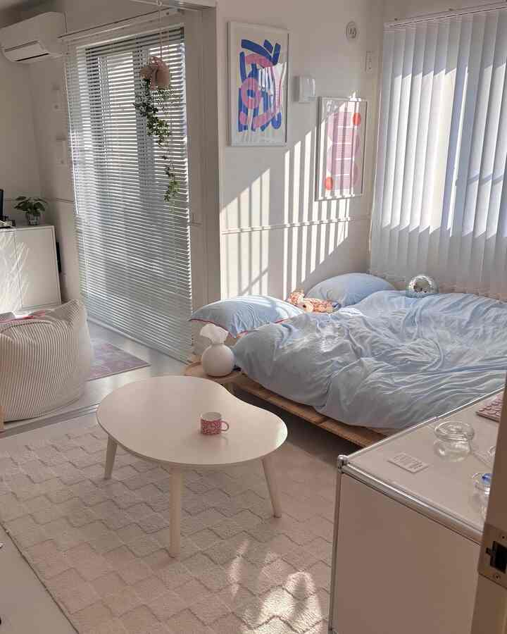 明るい白とベージュ調の寝室、低いベッドとブラインド、丸いテーブルやビーンバッグが配置された落ち着いたナチュラルモダンなインテリア