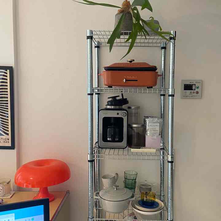 Dim-toned studio living room with metal shelving featuring bright orange kitchen appliances and potted plant