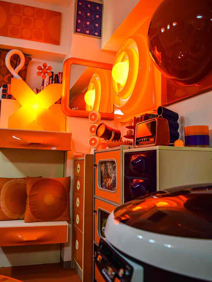 温かみのあるオレンジ色調のレトロなリビング、特徴的な照明とビンテージ家具が配置された雰囲気のあるインテリア