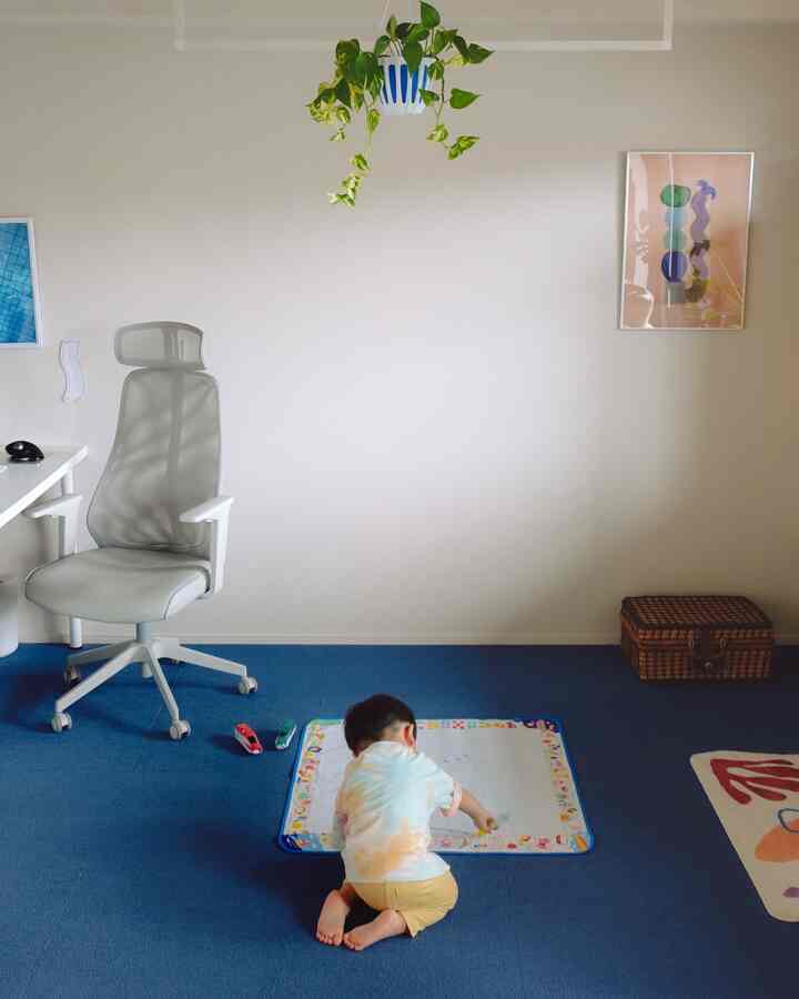 青いカーペットと白いオフィスチェアのあるシンプルな子供部屋、床のマットで絵を描く子供がいる雰囲気のあるインテリア