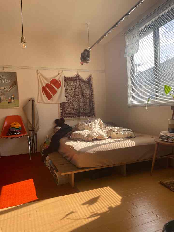 木目調の床と明るいホワイトの壁が調和する一人暮らしの寝室、ミッドセンチュリーモダンスタイルのオレンジチェアが印象的な居心地の良い空間