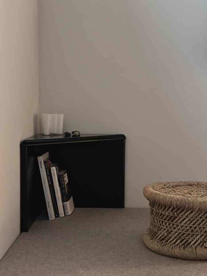 ナチュラルカラーの床と黒いコーナー収納が配置されたモダンなリビングの一角にラタン製のスツールが置かれた落ち着いた空間