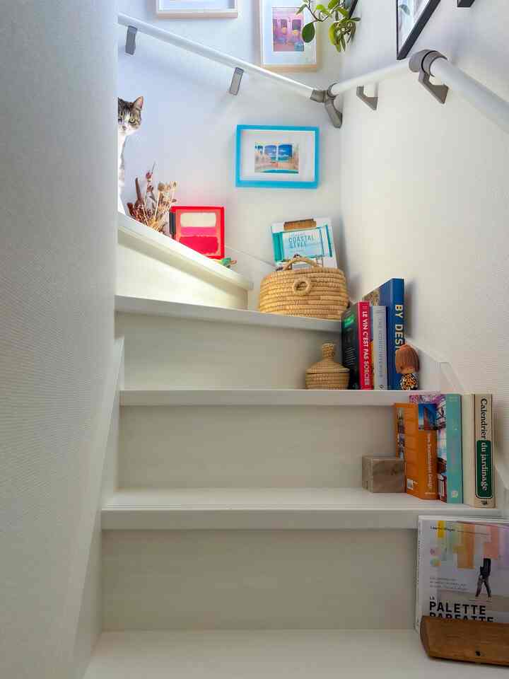 明るいナチュラルカラーの階段空間、本と額縁、猫がいる温かみのある雰囲気のインテリア