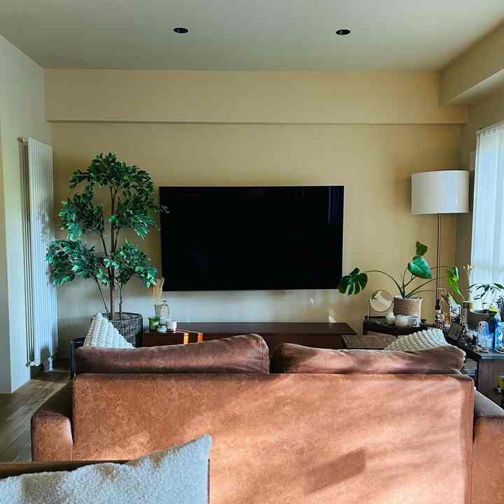 Modern living room with beige walls and brown sofa, featuring artificial plants and a floor lamp in a cozy setting