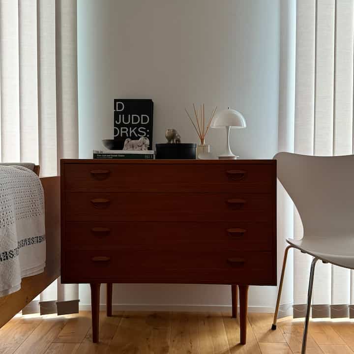 木目調とホワイトが調和するリビング空間、カイクリスチャンセンのヴィンテージチェスト、白い椅子と照明が配置された清潔感と暖かみのあるインテリア