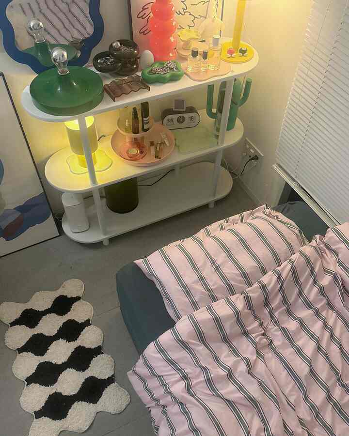 ピンクとグリーンの色調が調和した8畳の寝室、ベッドと棚が配置された落ち着いたモダンな一人暮らし空間