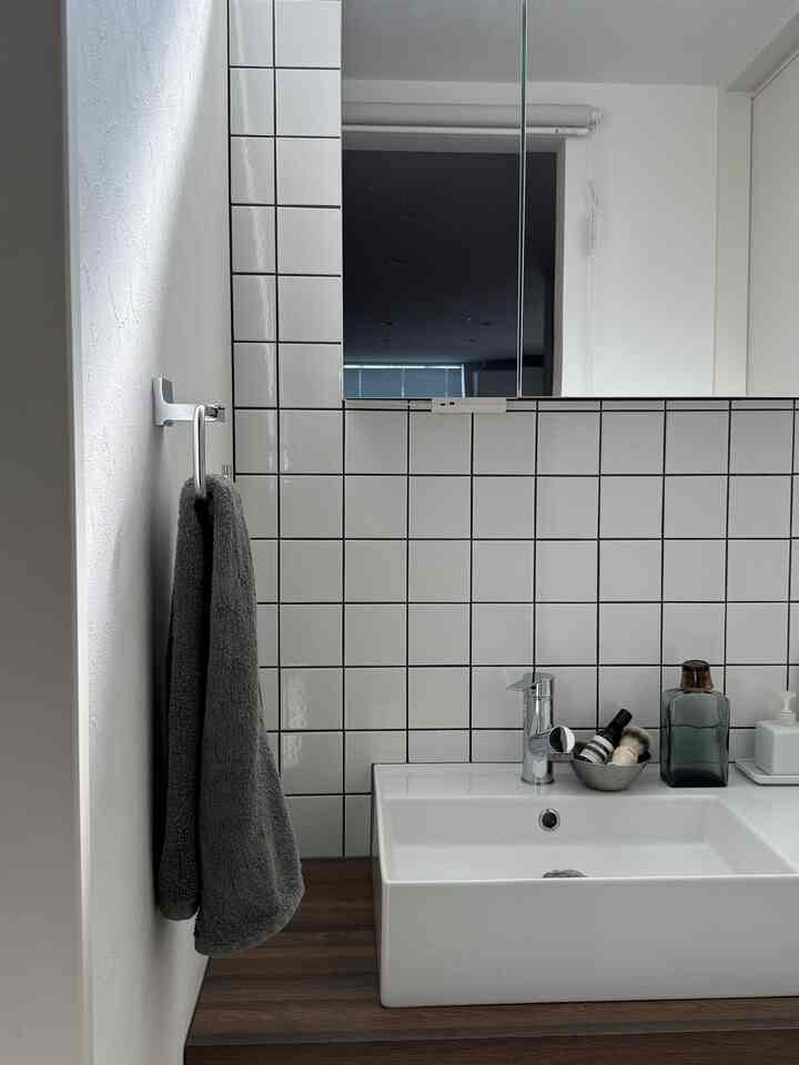 ホワイトとナチュラルトーンのバスルーム、シンプルな洗面台と鏡、グレーのタオルが調和した雰囲気のあるインテリア