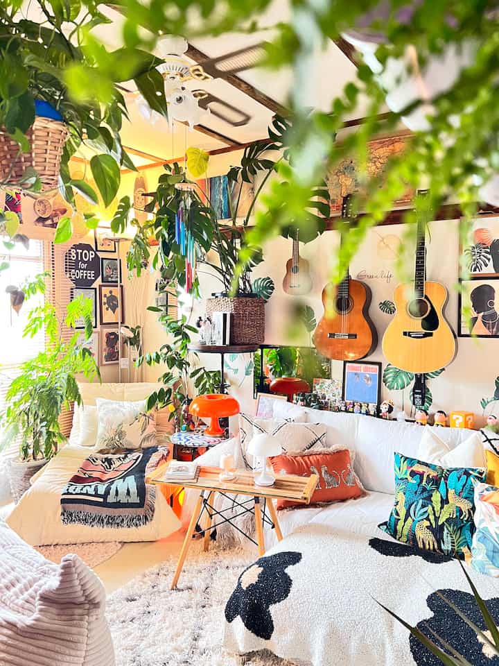 ホワイトとナチュラルな色調のリビング、多様な植物とソファ、テーブルランプが配置された雰囲気のある空間