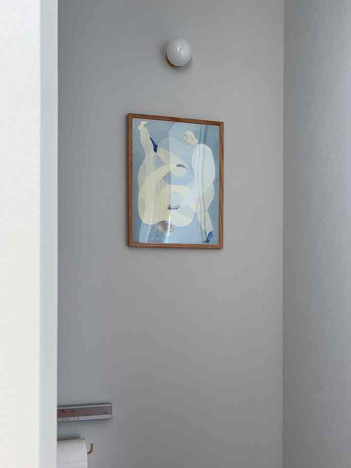 Simple bathroom in white and beige tones featuring abstract wall art and wall sconce centered on the wall