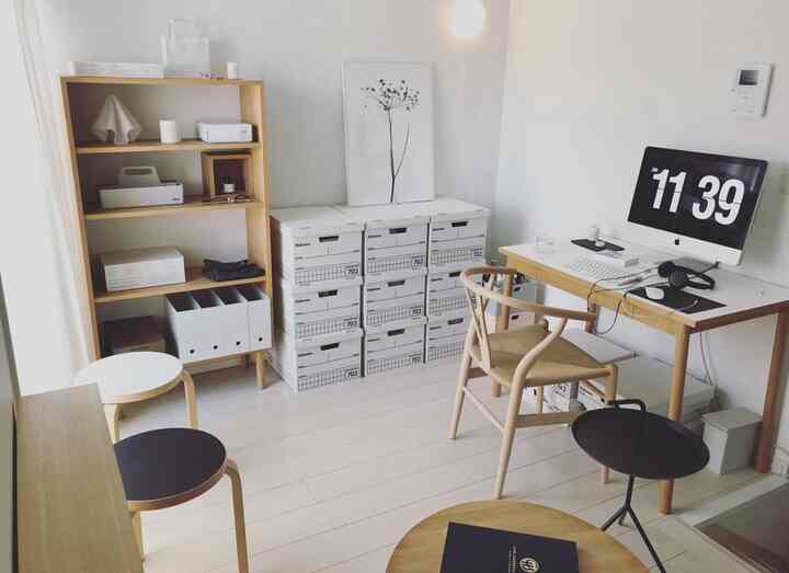 白と木目調の調和が美しいミニマルなワンルームのホームオフィス、デスク、椅子、整理された収納箱が配された雰囲気のあるインテリア。