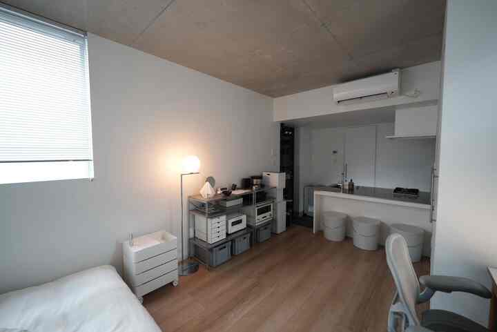 白と木目調のワンルームリビング、ミニマルな家具とホームオフィスが配置された印象的な空間