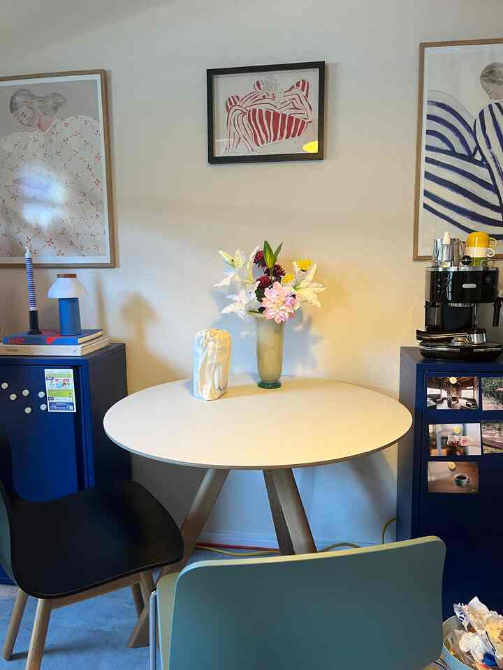 柔らかいホワイトとブルーの色調のダイニング、丸テーブルに二色の椅子、花瓶とコーヒーマシンが調和したミニマルな空間