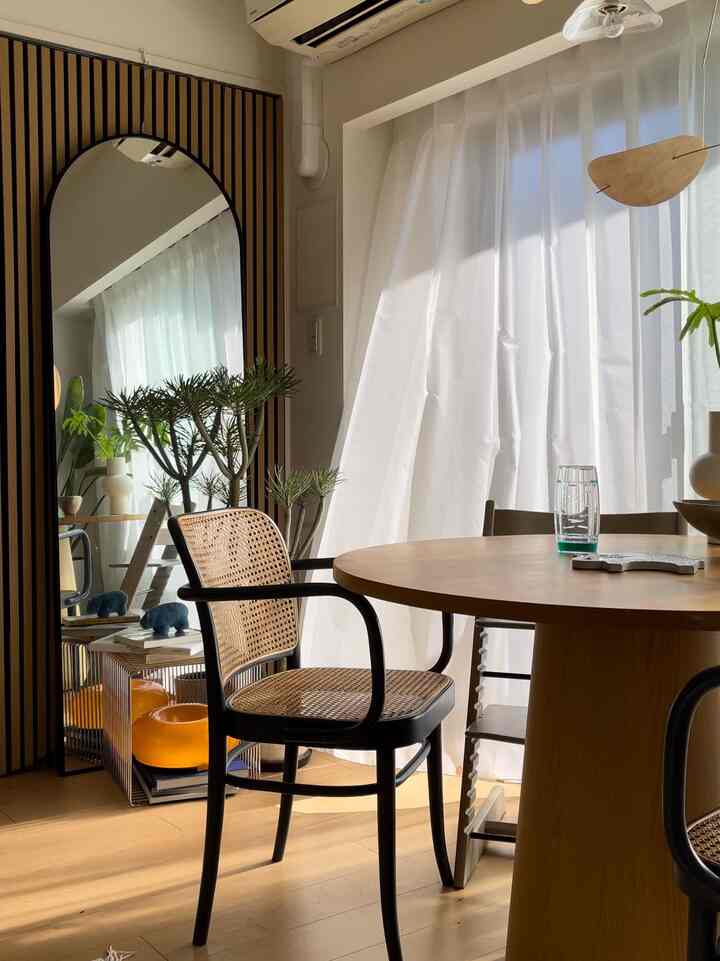 自然なライトブラウンの色調が特徴のダイニングルーム、大きなアーチ型の鏡と明るいカーテンが配置された暖かなインテリア