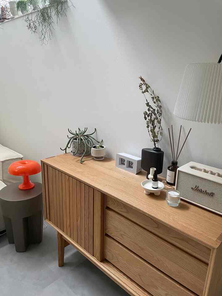 白い壁と木目調のキャビネットが調和したリビングの一角、オレンジのテーブルランプとホワイトのフロアランプが配置されたインテリア