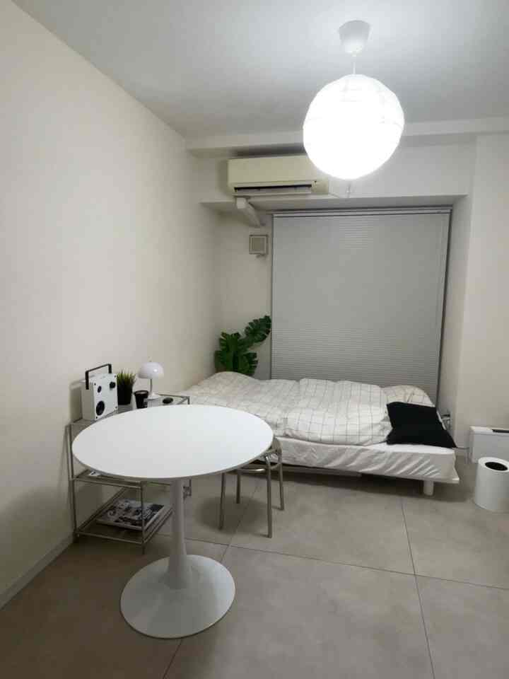 ホワイトとグレーのモノトーンの一人暮らし用寝室、丸いダイニングテーブルとシンプルな収納棚が配置された印象的な空間