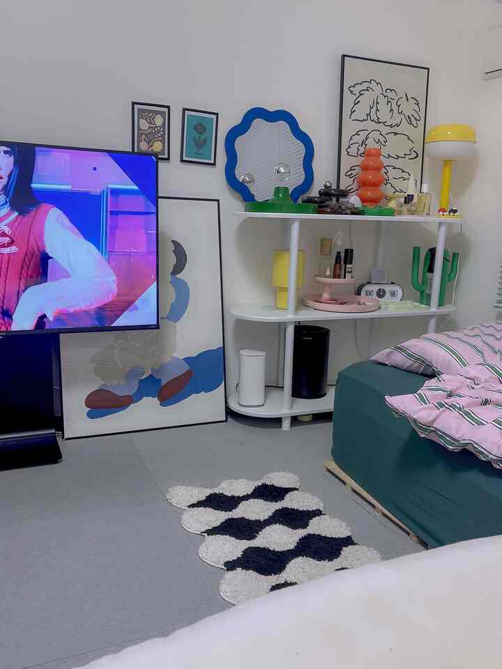 白い壁とモダンな棚、ピンクとグリーンの寝具が配置された8畳のワンルーム寝室のインテリア