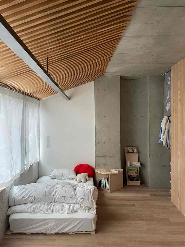 A small bedroom with natural wood tones and white walls, featuring a simple bed and storage, creating a minimalist atmosphere