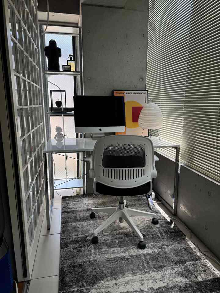 モノトーン調の狭いホームオフィス、白いデスクとオフィスチェア、棚とラグが配置された印象的な空間