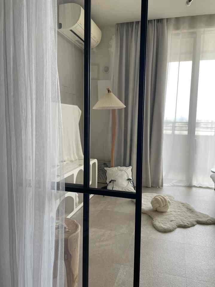 明るくナチュラルな色調のリビング、広いカーテンとフロアランプ、ラグが配置されたすっきりとした空間