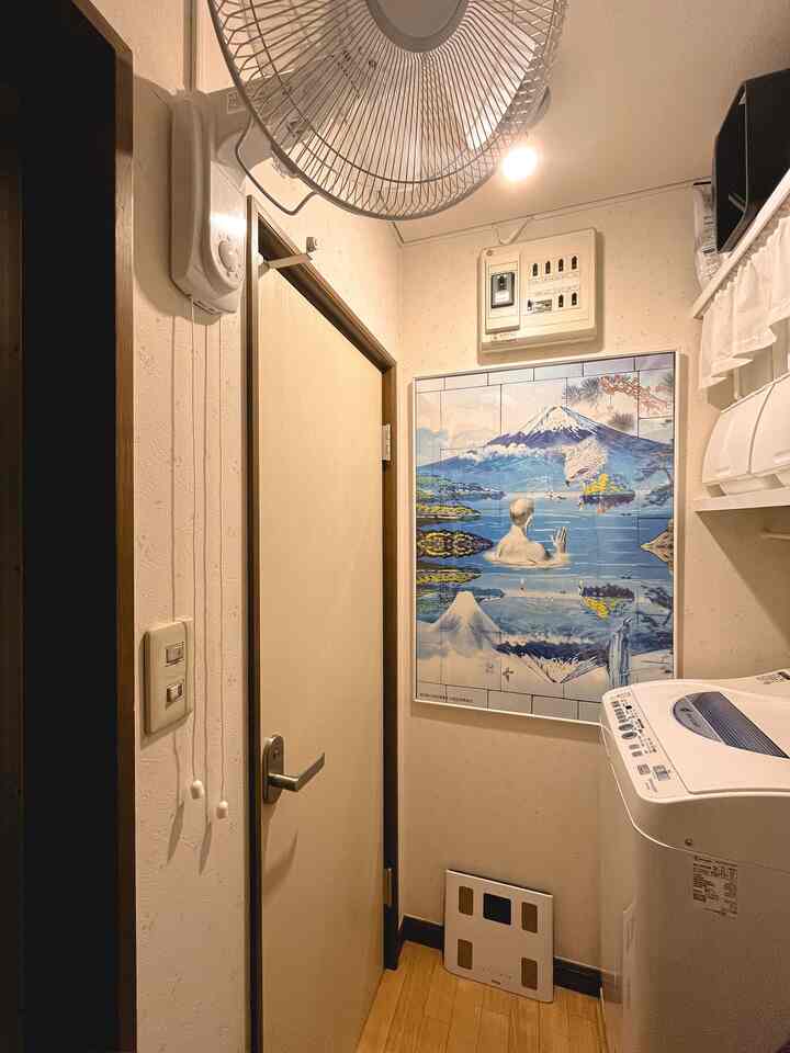 アイボリーとブラウンのトーンの小さな玄関スペース、壁にポスターと洗濯機が配置された落ち着いた雰囲気のインテリア