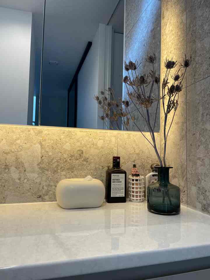 Beige marble wall and white vanity in bathroom featuring blue vase with dried flowers in a modern style interior