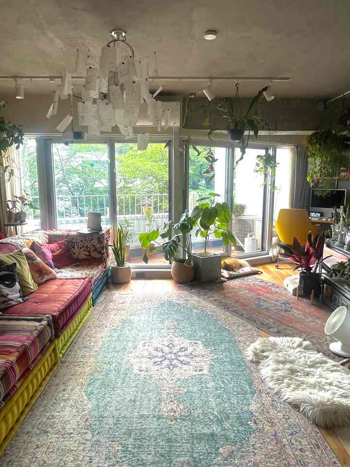 温かみのある木目調の床とカラフルなソファ、多様な観葉植物が配置された活気あるヴィンテージ調のリビングルーム