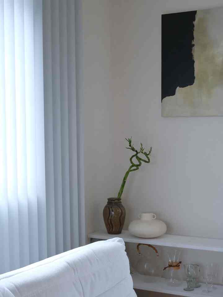 明るいホワイトトーンのリビング、棚にガラス食器と陶器が並び、ソファの前には植物が配置されたナチュラルなインテリア