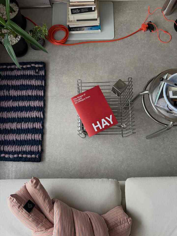 グレーの床と白いソファがある1LDKのリビング、赤いHAYの本とクッション、ドアマットが配置された落ち着いた空間