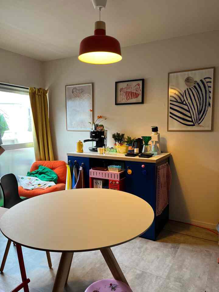 黄色と青のトーンが特徴的なリビング、白い丸テーブルと青いキャビネット、赤いペンダントライトが配置された雰囲気のある空間