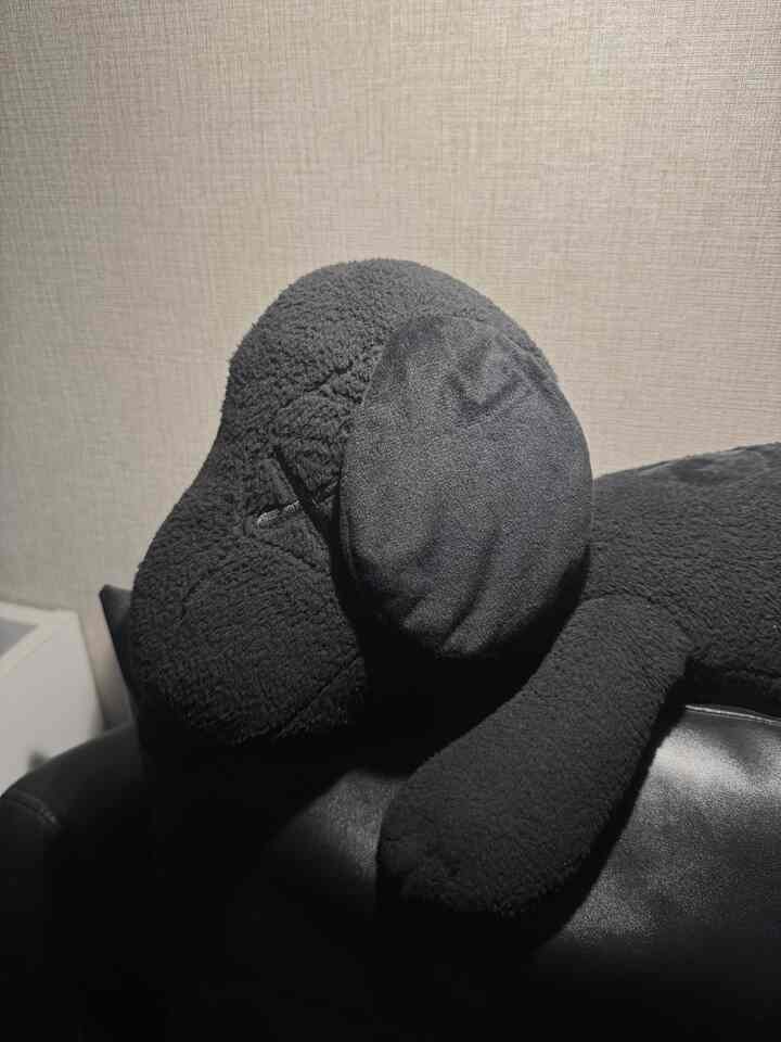 黒いソファの上に置かれた黒い犬の形をした柔らかいペットベッドとテクスチャのある壁の背景