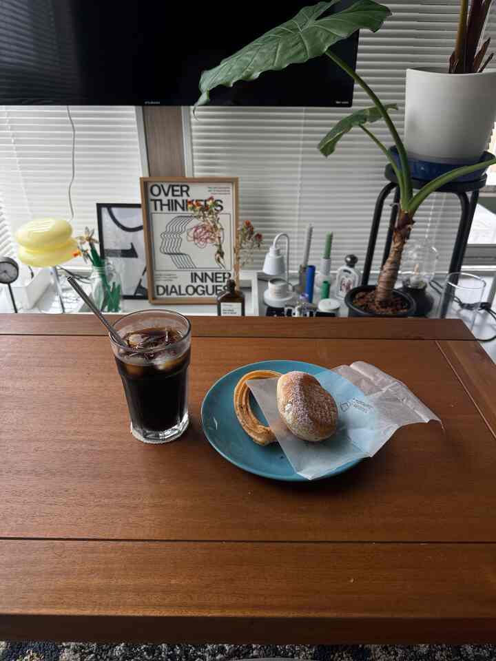 ナチュラルカラーのブラウン木製ローテーブルにホームカフェ風のアイスコーヒーとドーナツが置かれた、落ち着いたリビング空間